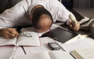 Totally desperate businessman with head on office desk top being overloaded with loads of work